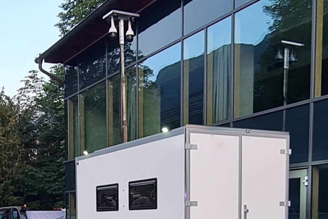 Mobile Sicherheitslösungen Weiße Container vor einem modernen Gebäude mit großen Glasfenstern.